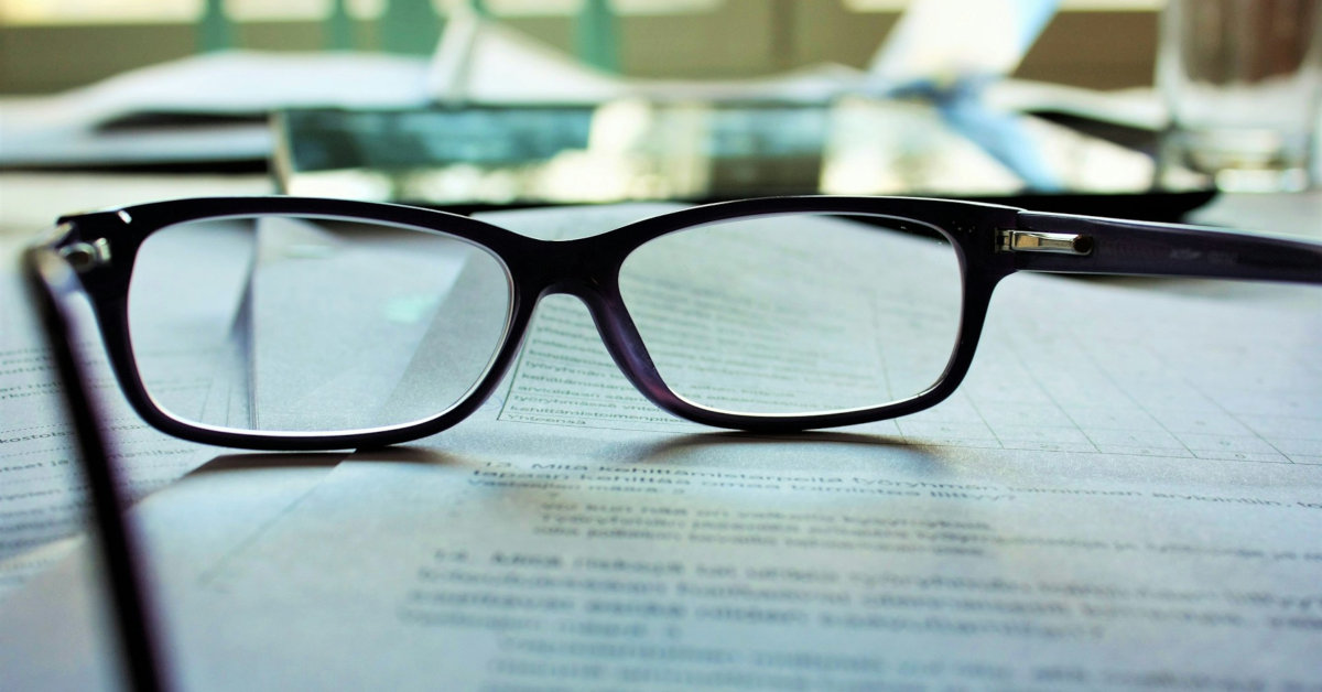 Läsglasögon placerade på en öppen bok. - Blanc Reading