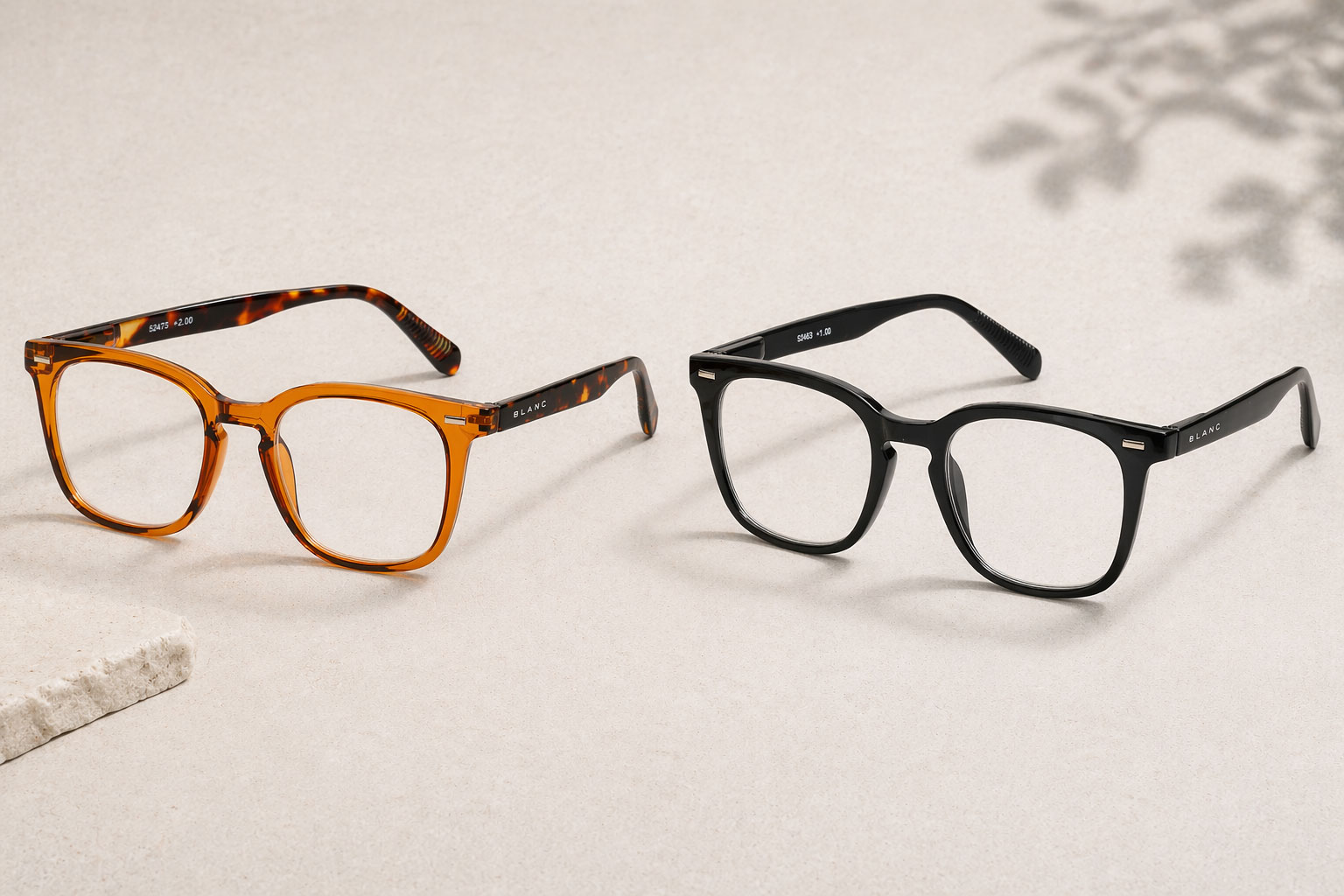 Två par läsglasögon visas på en ljusbeige yta. Det ena paret har ett sköldpaddsmönster och det andra paret är helt svart. Båda paren har fyrkantiga bågar och klara linser.