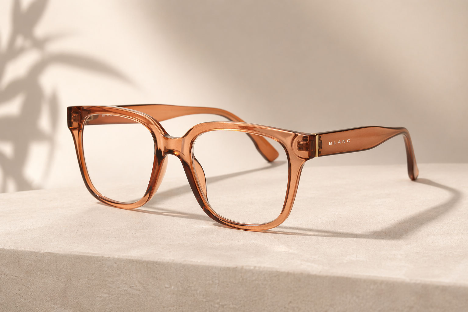 Ett par genomskinligt bruna läsglasögon med tjocka fyrkantiga bågar vilar på en ljusbeige stenyta. Ordet "BLANC" är tryckt i vitt på skalmen. Bakgrunden är neutral med en mjuk skugga.